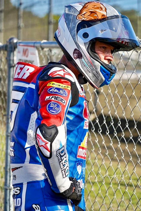 Texter staring at a track through a fence with his helmet and gear on.